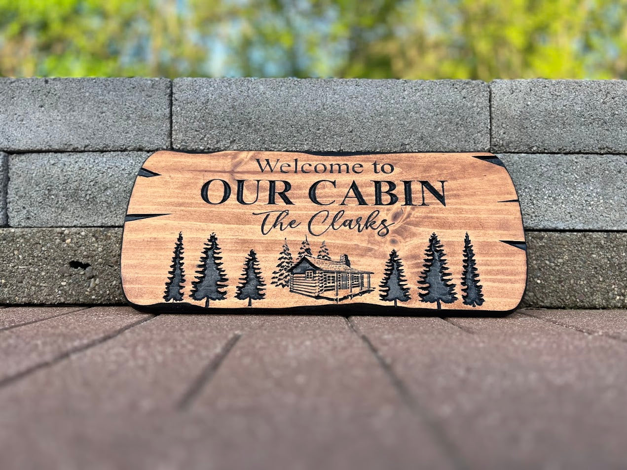 A personalized wooden cabin sign with engraved text and images, placed on a brick surface.